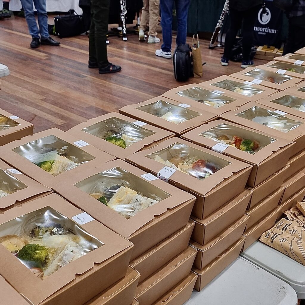 150 gourmet lunch boxes prepared for an event, stacked on tables with eco-friendly packaging.