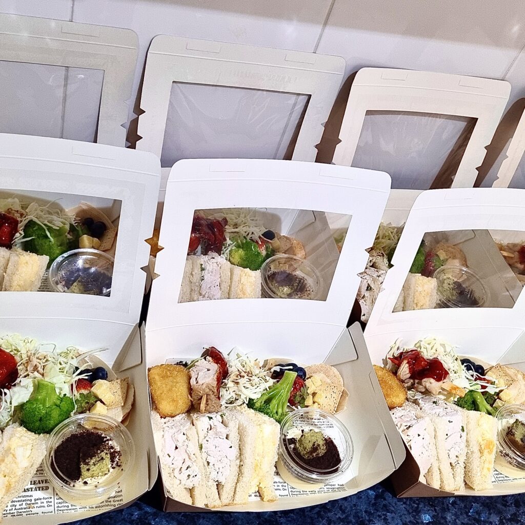 Prepping gourmet lunch boxes with sandwiches, salad, and desserts for catering.