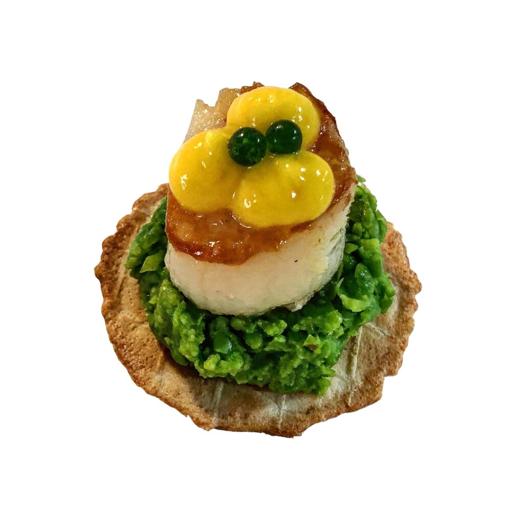 Gourmet canapé with cracker, mashed peas, seared scallop, corn puree, and parsley caviar for elegant catering events.