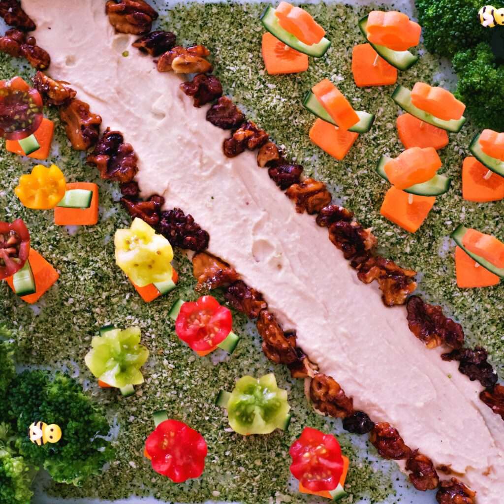 Garden-themed crudités platter for kids, featuring colorful vegetable flowers, broccoli trees, and hummus soil, perfect for parties and events.